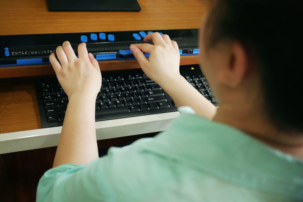 View of a student using a braille terminal next to a keyboard.