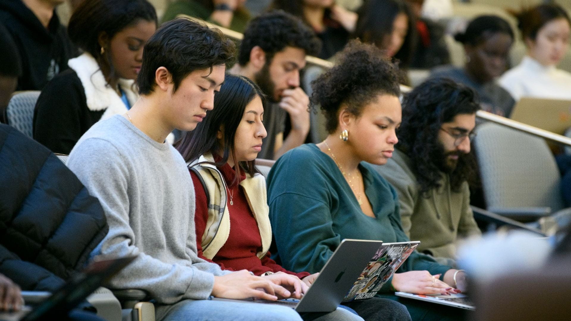 Students look down at their laptops in a lecture hall.